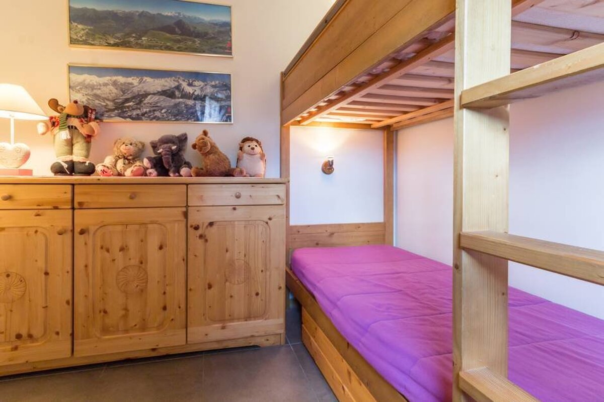 A bunk bed with purple sheets and a dresser with stuffed animals on it