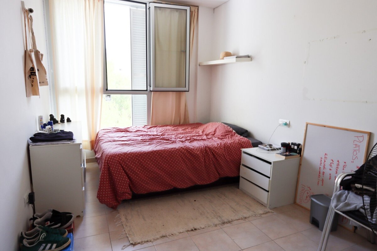 A bedroom with a bed a nightstand and a whiteboard that says ' pilates ' on it