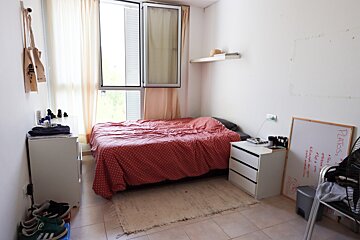 A bedroom with a bed a nightstand and a whiteboard that says ' pilates ' on it