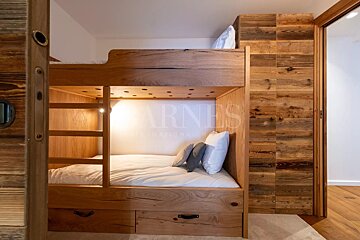 A modern rustic bedroom featuring custom wooden bunk beds with integrated lighting and storage, alongside warm wood paneling and white bedding.