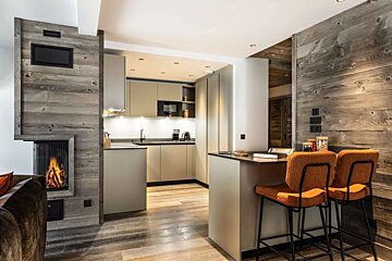 A sleek, modern kitchen and dining bar with orange stools, integrated into a warm space featuring rustic wood walls and a fireplace.
