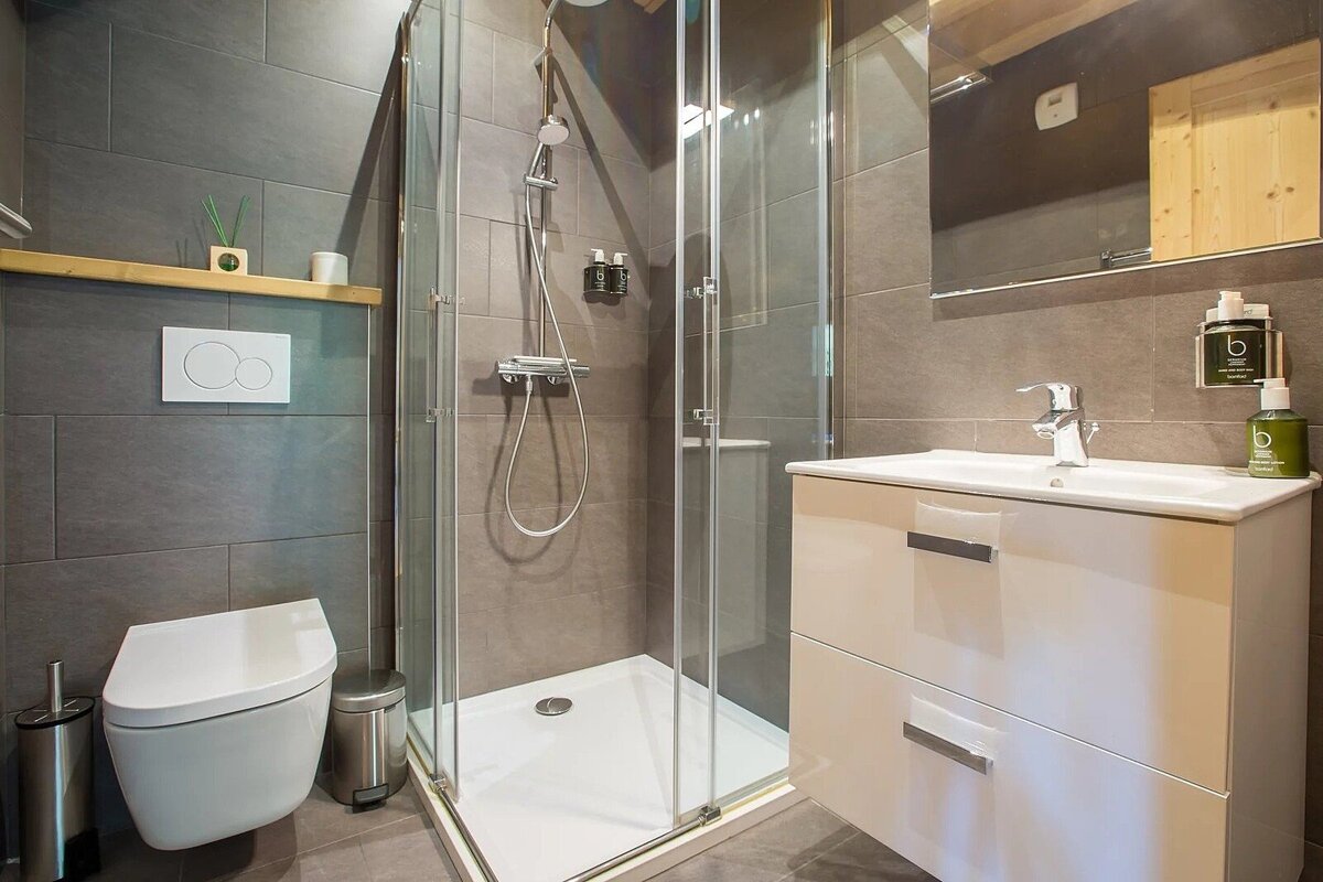 A modern, tiled bathroom with a glass-enclosed shower, a wall-mounted toilet, and a vanity with a sink and mirror. The decor is sleek and minimalist.