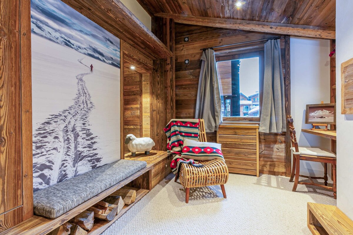 A warm, rustic ski chalet interior with extensive wood paneling, a large snowy mountain mural, cozy seating, and a window view, evoking a serene alpine retreat.
