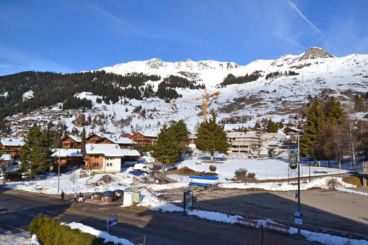 A snowy alpine village with wooden chalets nestled below majestic snow-capped mountains under a clear blue sky.