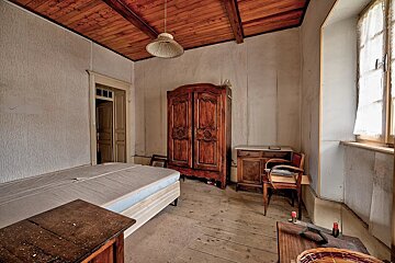Dusty, aged room with wooden ceiling & floor, a bed, vintage wardrobe, dresser, and a window with lace curtains.