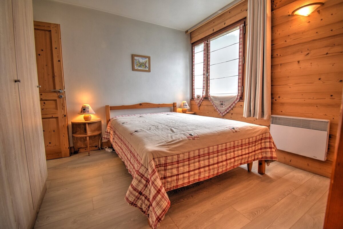 Cozy rustic bedroom featuring a double bed with a red plaid bedspread, wooden paneling, and warm lighting from bedside lamps.