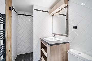 A bathroom with white tiles and a sink and mirror