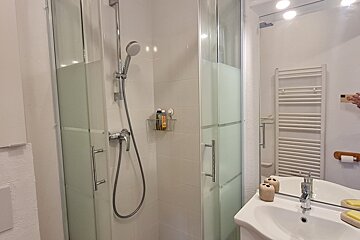 A modern white bathroom showcasing a shower cabin with frosted glass, a sink under a mirror, and a white towel warmer.