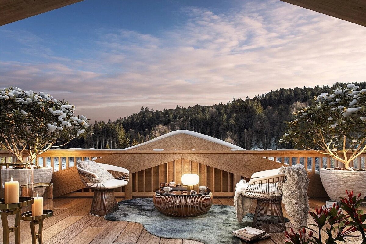 A cozy winter terrace with stunning mountain views, featuring comfortable seating, a lit table, and snow-dusted plants under a soft sky.