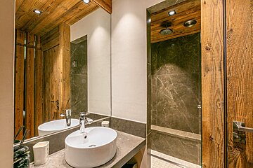 A modern bathroom featuring a rustic wooden ceiling, a white vessel sink on a stone vanity, and a sleek marble shower.