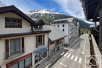 An elevated view of a mountain town street with alpine buildings and snow-capped peaks in the background.