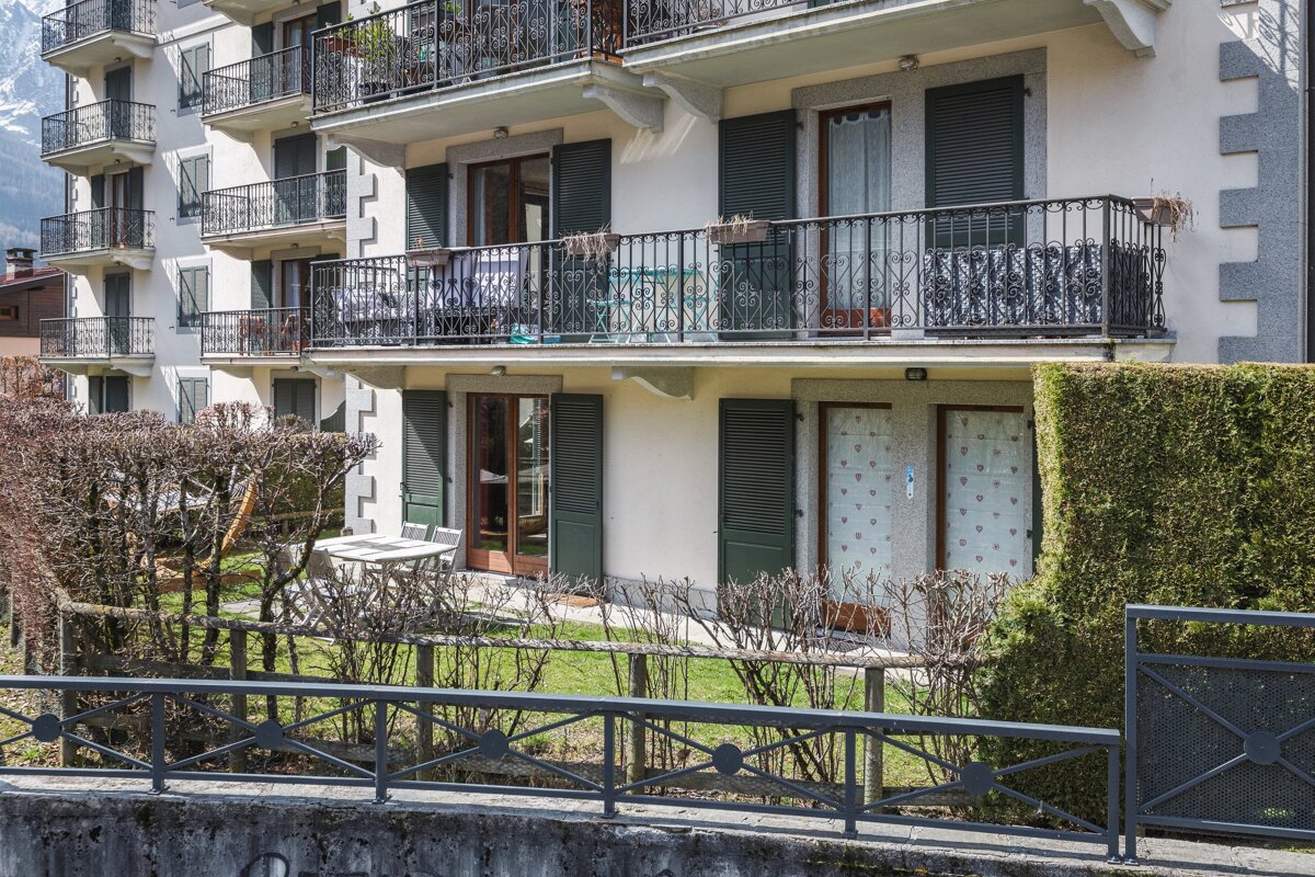 A building with green shutters has a balcony with a table and chairs on it