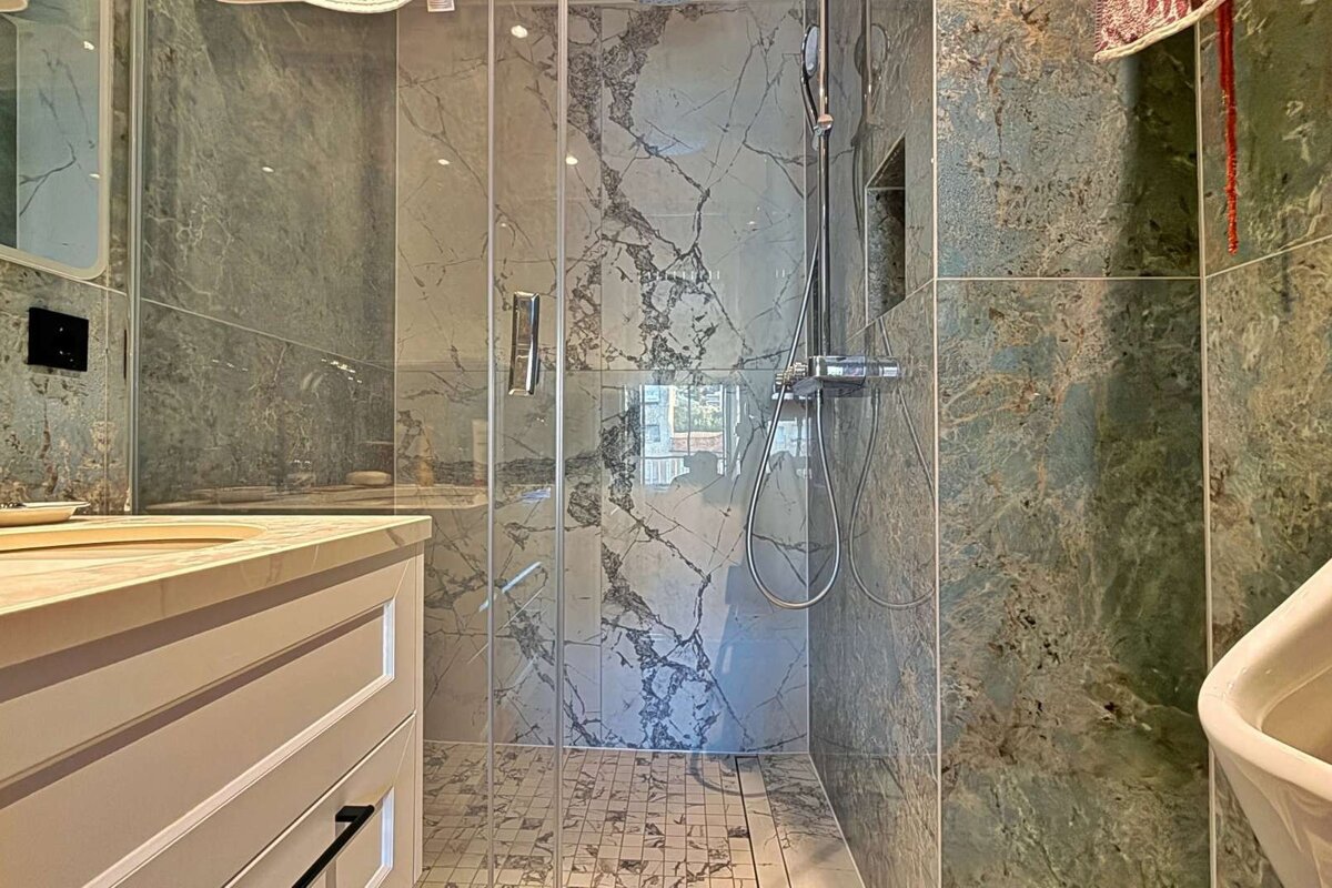 A modern bathroom features a glass shower enclosure, gray and green marbled walls, and a vanity with a sink.