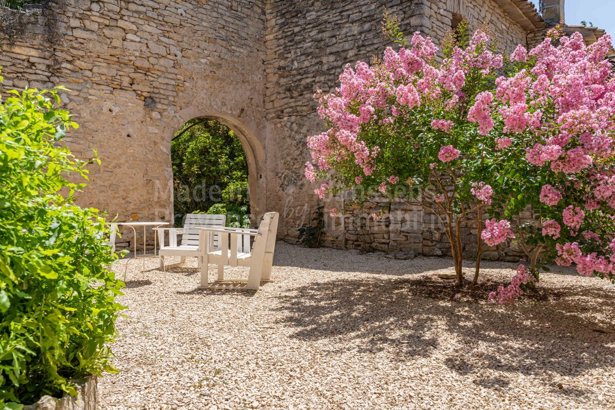 A white chair sits under a tree with pink flowers in front of a stone wall