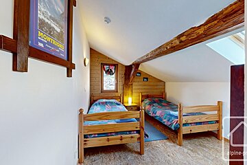 Cozy attic bedroom with two wooden single beds, colorful bedding, wood paneling, an exposed beam, window, and a ski poster on the wall.