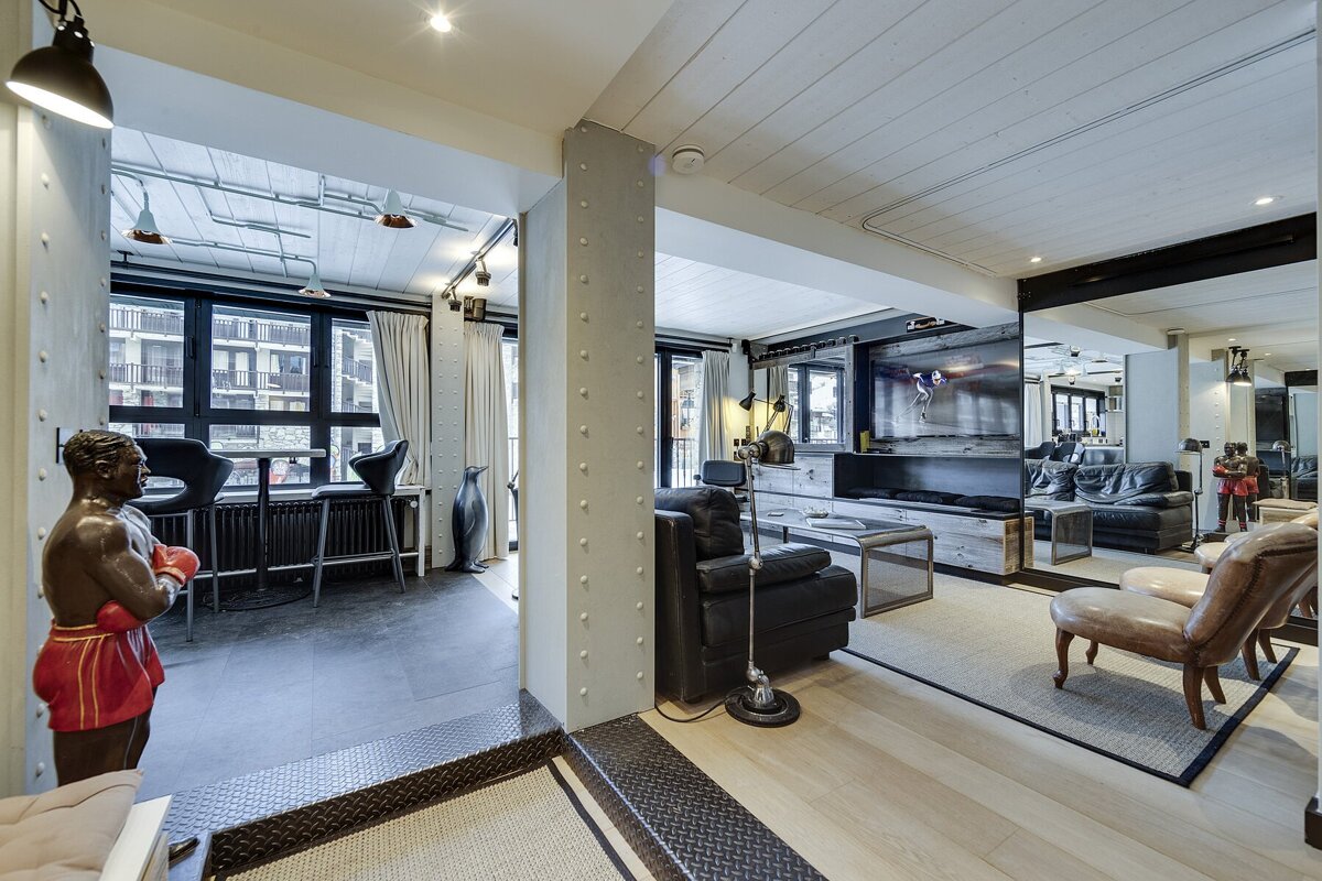 Industrial-chic loft interior with a living room, bar area, mirrored walls, and unique decor like a boxer statue and a penguin.