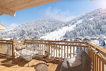 A cozy wooden balcony with chairs and string lights overlooks a stunning snowy mountain landscape with pine trees, a ski slope, and a village.