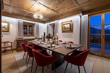 A dining room with a long table and red chairs