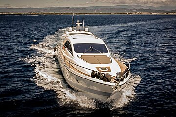 A large yacht is floating in the ocean with mountains in the background