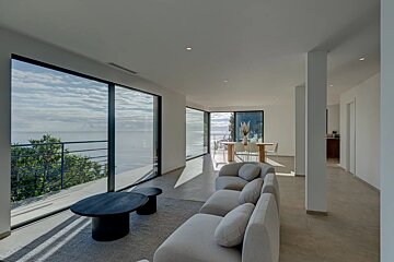 A modern, minimalist living room with floor-to-ceiling glass windows offering panoramic ocean views.