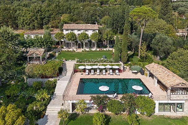 Aerial view of a luxury villa with a large pool, lounge chairs, and manicured lawns, surrounded by lush green trees.