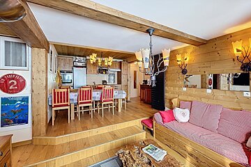 Cozy, rustic, split-level chalet-style living area featuring wood paneling, a dining table with red chairs, a kitchen, and a wooden sofa.
