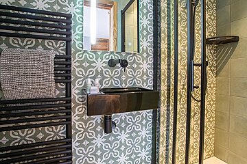 Modern bathroom with green patterned tiles, a black wall-mounted sink, a black towel radiator, and a glass shower door.
