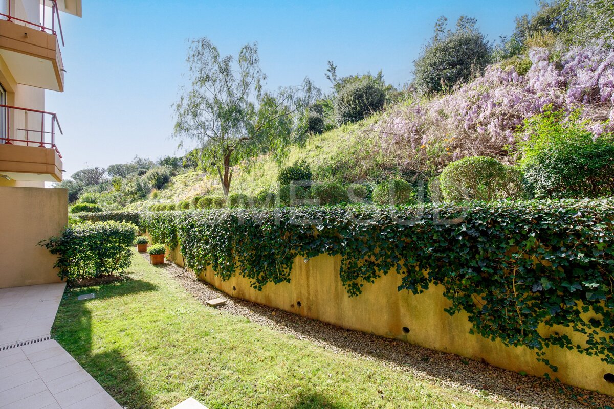 A lush green lawn surrounded by trees and bushes with a building in the background