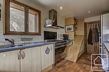 Cozy kitchen with a mountain view window, light wood cabinets, stainless steel stove, tiled floor, and a unique wooden storage unit.