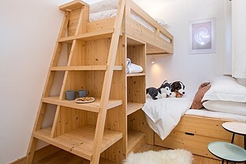Cozy wooden bunk beds with a built-in shelving ladder, white bedding, and stuffed animal dogs on the lower bed.