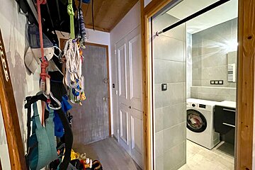 A hallway with climbing gear and skis on the left, leading to a modern tiled laundry room with a washing machine and a doorway pull-up bar.