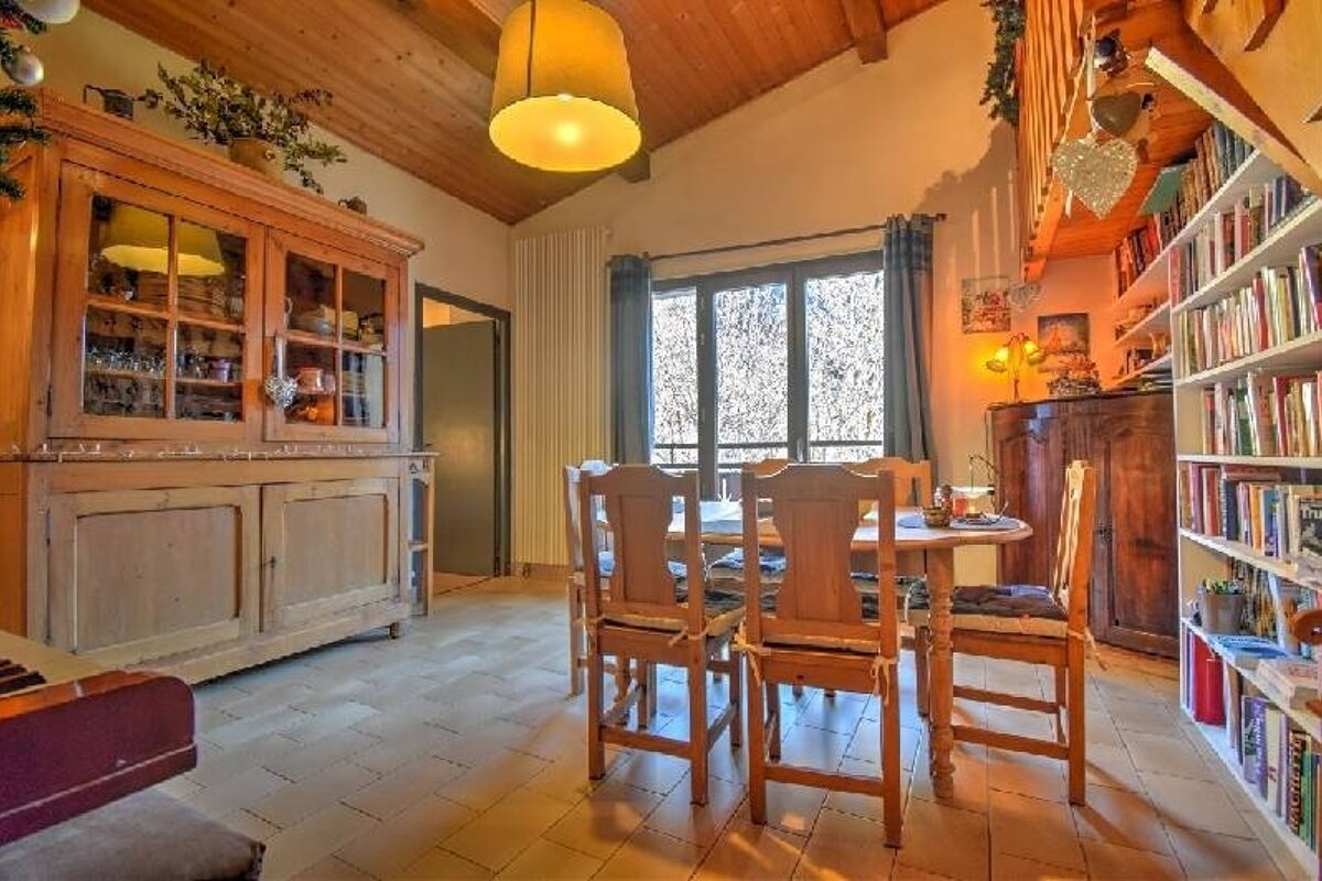 Warm, rustic dining room featuring a wooden table and chairs, a large vintage cabinet, filled bookshelves, and cozy cabin-style lighting.