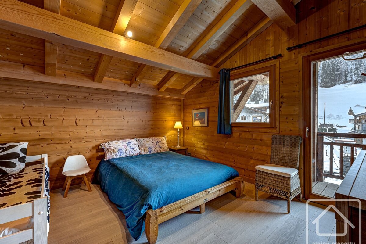 Cozy, rustic wooden bedroom with a blue bed, bunk bed, and a balcony overlooking a snowy alpine landscape.