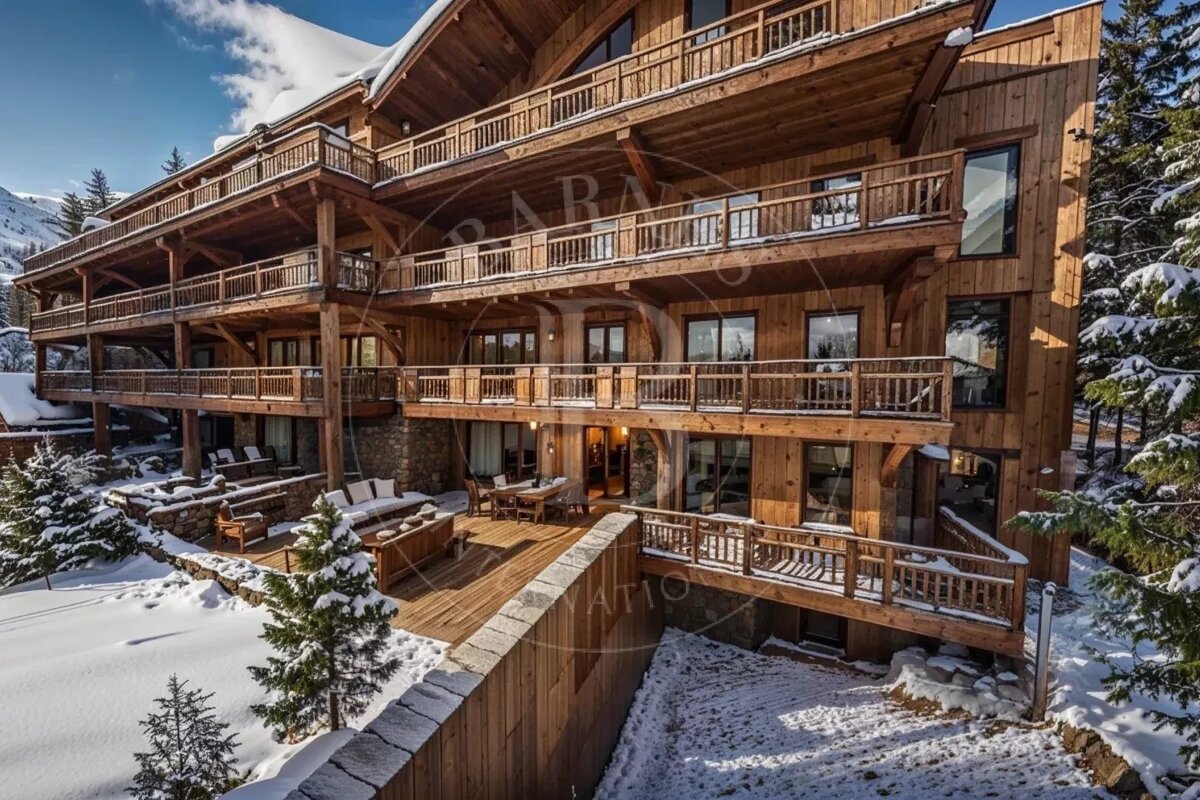 A multi-story wooden ski chalet with balconies, surrounded by snow and pine trees on a sunny day.
