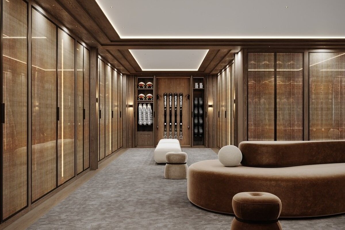 A lavish walk-in closet with wood and rattan wardrobes, featuring a central display for skis, helmets, and boots. Plush seating and warm lighting create an elegant space.