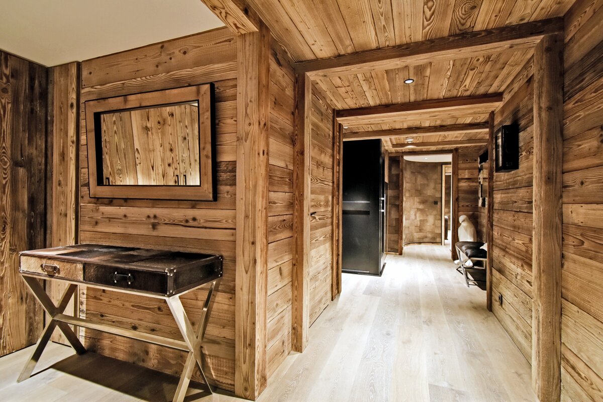 A rustic hallway with knotty wood paneled walls and ceiling, light wood floor, and a modern console table with mirror on the left.