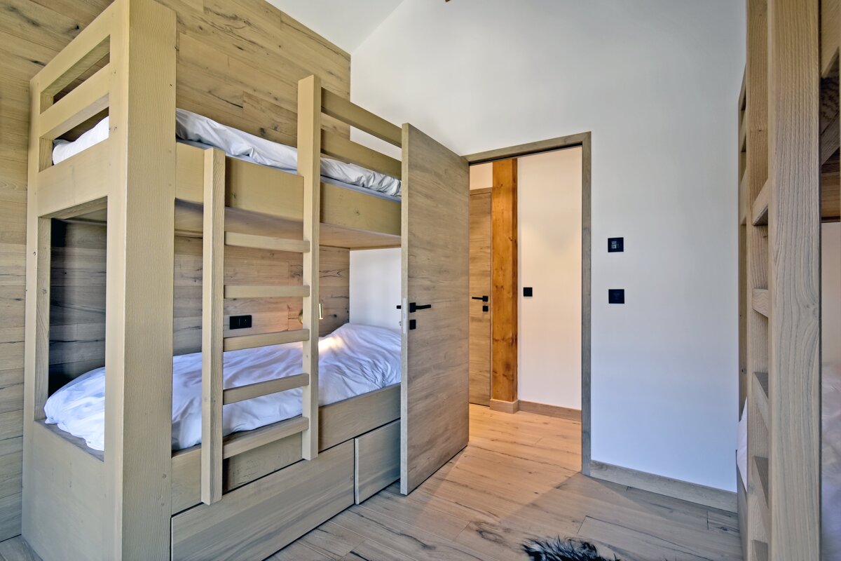 Modern light-wood bunk beds with storage drawers in a cabin-style bedroom, next to an open doorway.