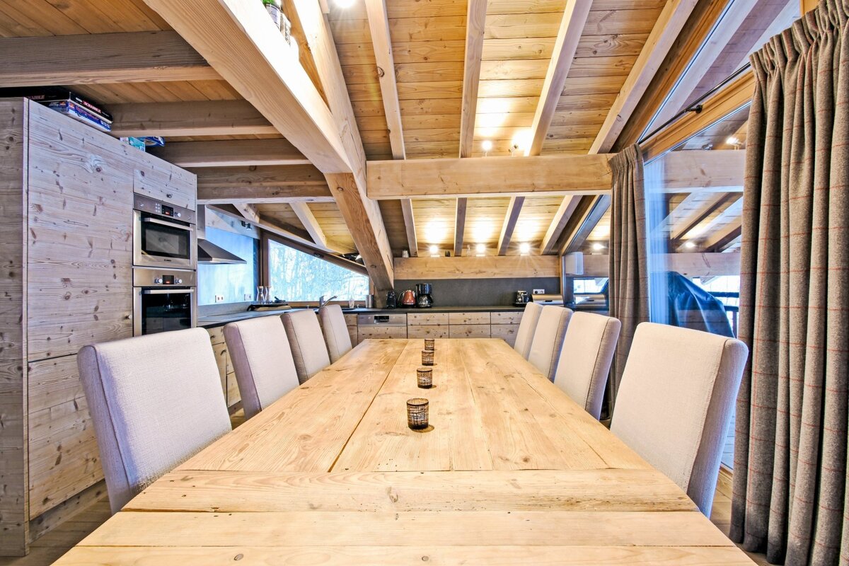 Cozy chalet dining room featuring a long wooden table, beige chairs, and rustic wooden walls and ceilings with exposed beams.