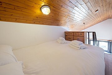 A bedroom with a wooden ceiling and a bed with white sheets