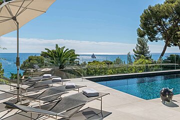 Sunny terrace with lounge chairs and a pool, offering a stunning view of the blue ocean with a yacht, under a clear sky.