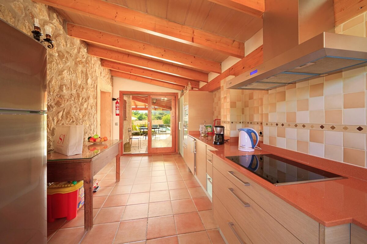 A modern kitchen with stone walls, wooden beams, tiled floor, and glass sliding doors opening to an outdoor area.