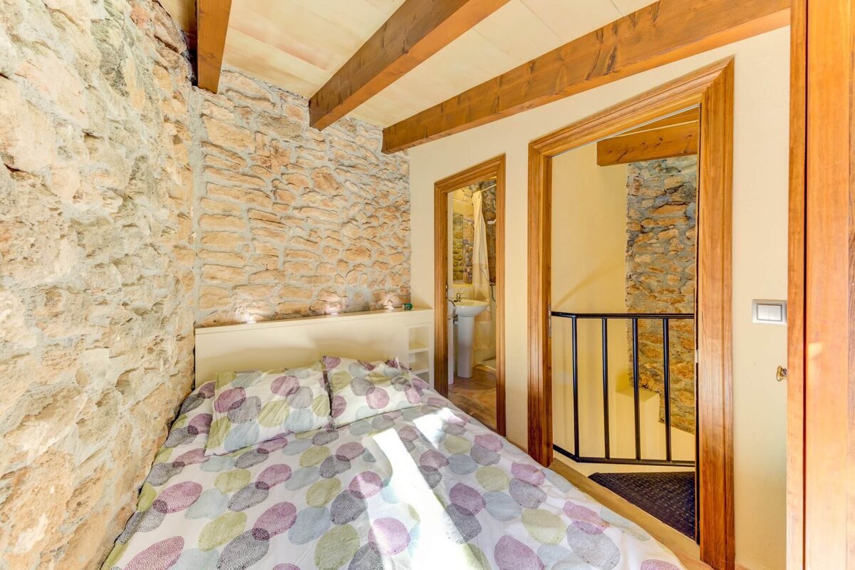 A small bedroom with a stone wall and a bed