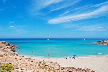 A group of people on a beach with a sailboat in the distance