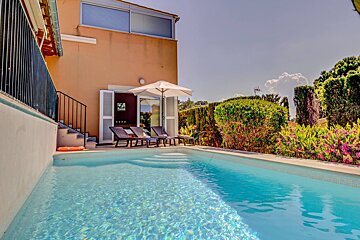 A swimming pool in front of a house with chairs and umbrellas