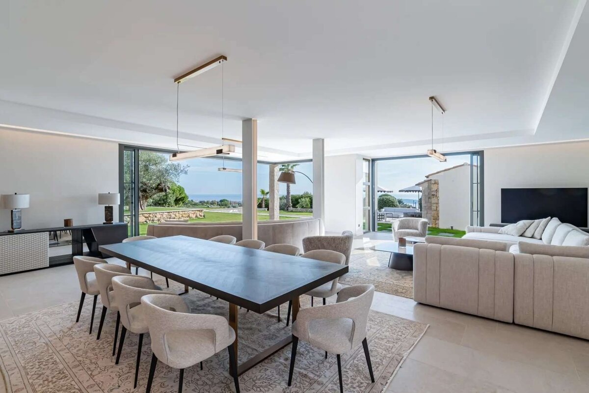 Modern open-plan living/dining room with stylish neutral furniture, large windows, and panoramic ocean views.