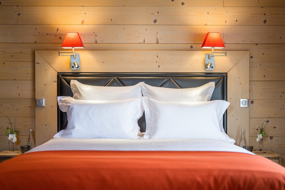 Cozy bed with white pillows and a red throw, set against a wood-paneled wall with two lit red reading lamps.