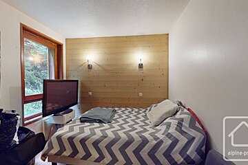A cozy bedroom with a bed featuring gray and white chevron bedding, a wood-paneled wall with sconces, a TV, and a window overlooking trees.