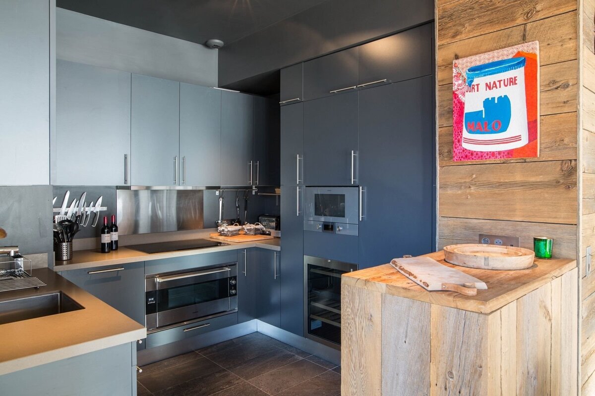 Sleek blue-grey modern kitchen with integrated appliances, contrasted by a rustic wood island and a vibrant pop art piece on a wood-paneled wall.