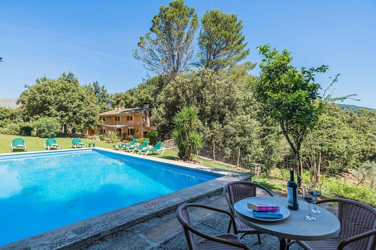 A table with a bottle of wine sits in front of a swimming pool