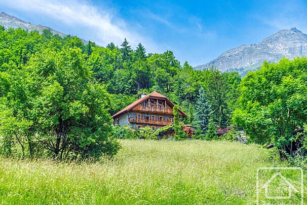 Beautiful wooden chalet amidst a vibrant green mountain landscape, featuring a sunny field and clear blue sky.